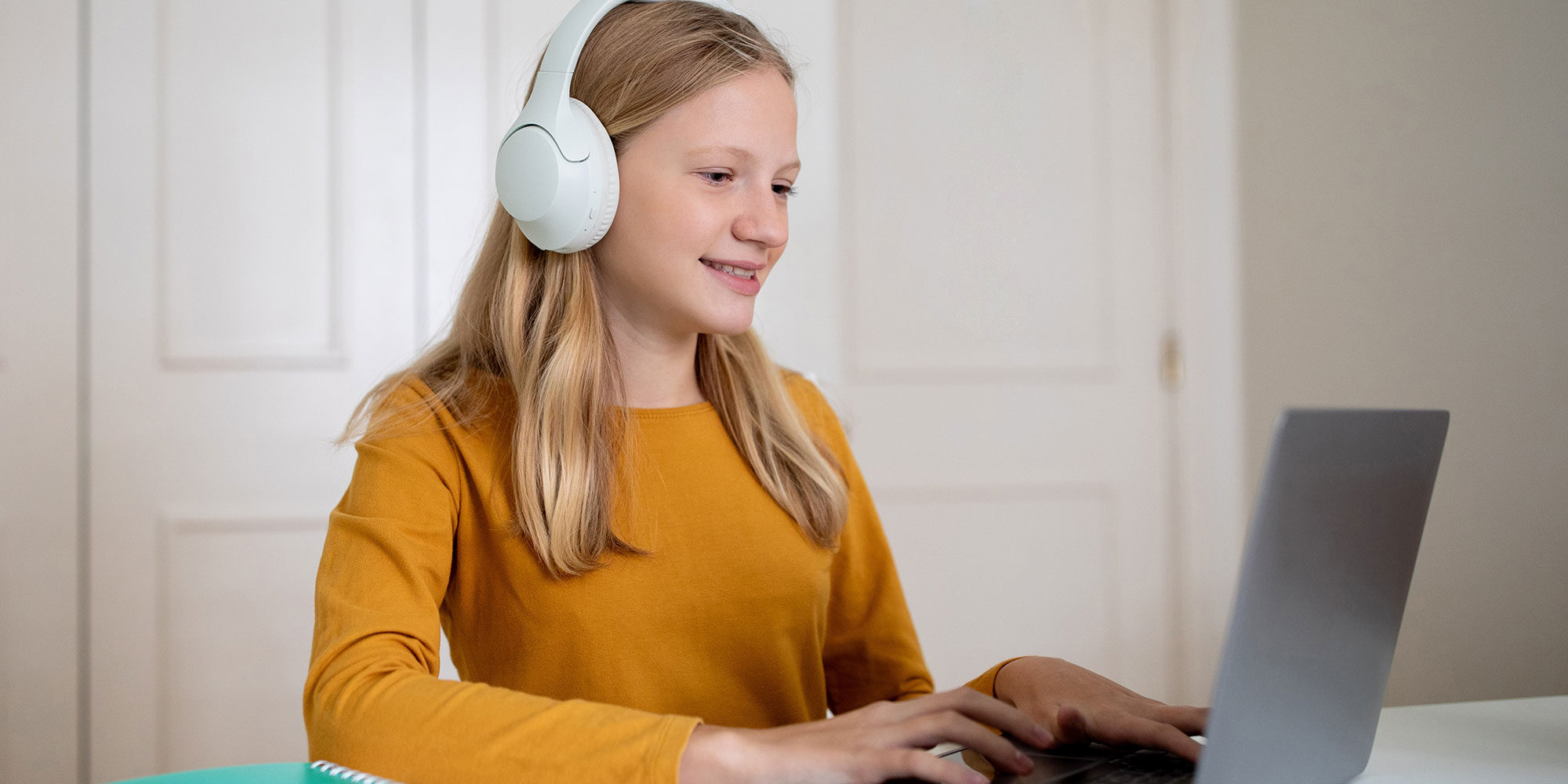 Young girl with headphones on typing on her laptop.