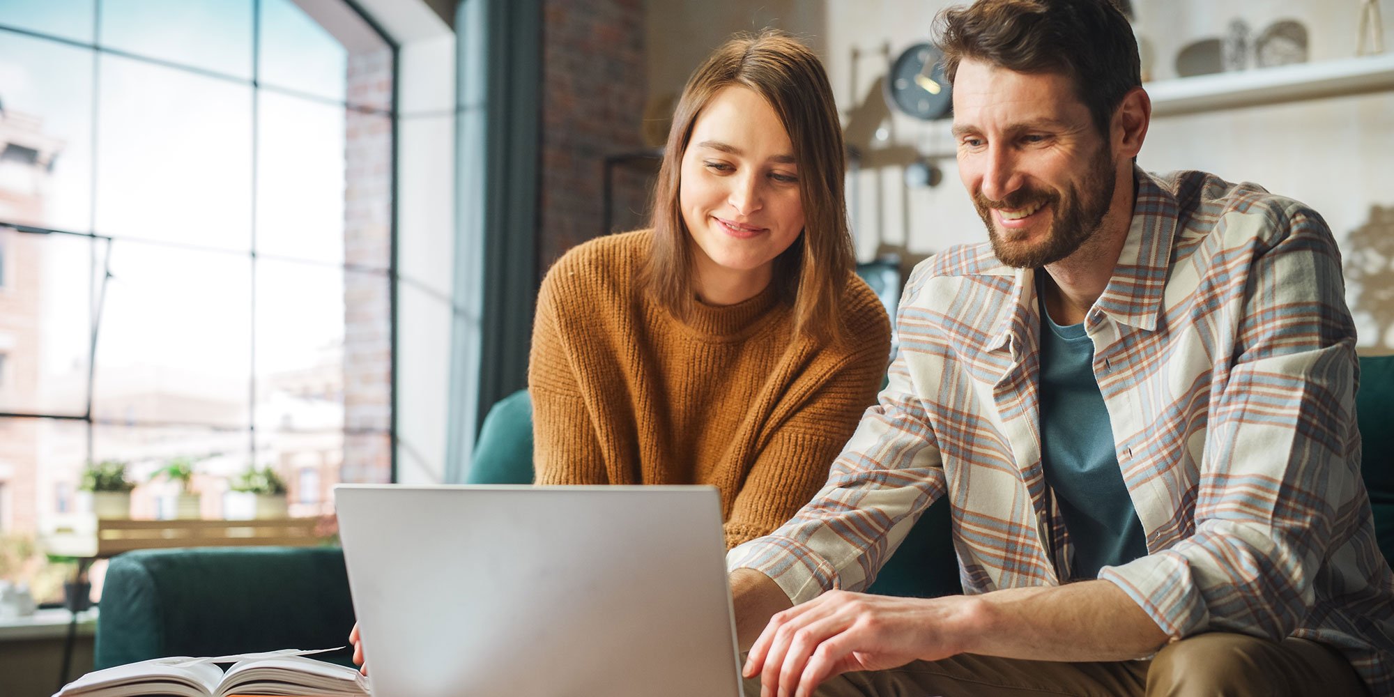 Couple smiling while using a laptop together at home.