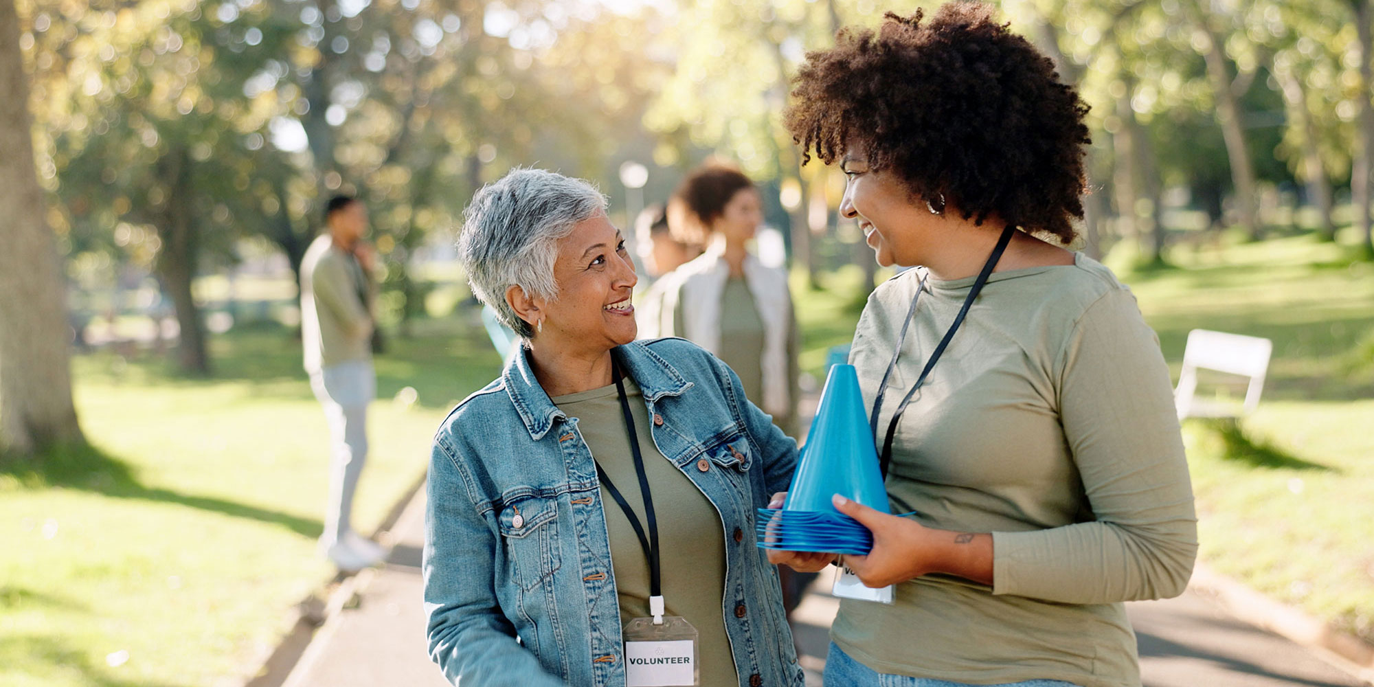 Two smiling volunteers holding blue cones and talking in a sunny park.