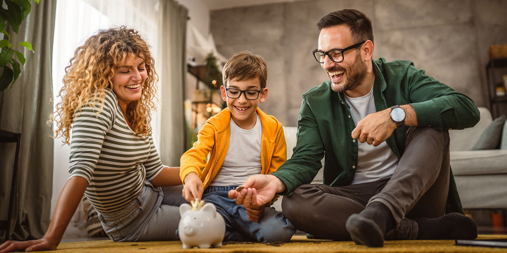 Family teaching young boy about saving by putting money in piggy bank.