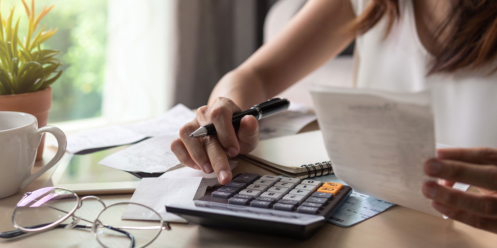 Person uses calculator and reviews receipts while budgeting at home.