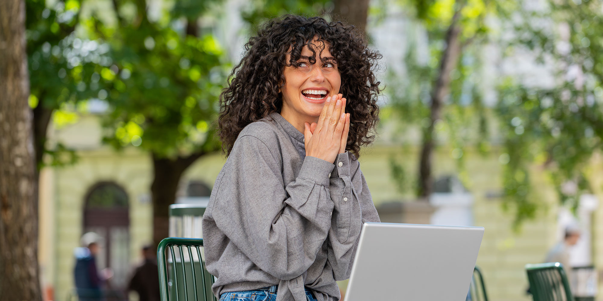 Smiling woman reacts joyfully while using a laptop outdoors.