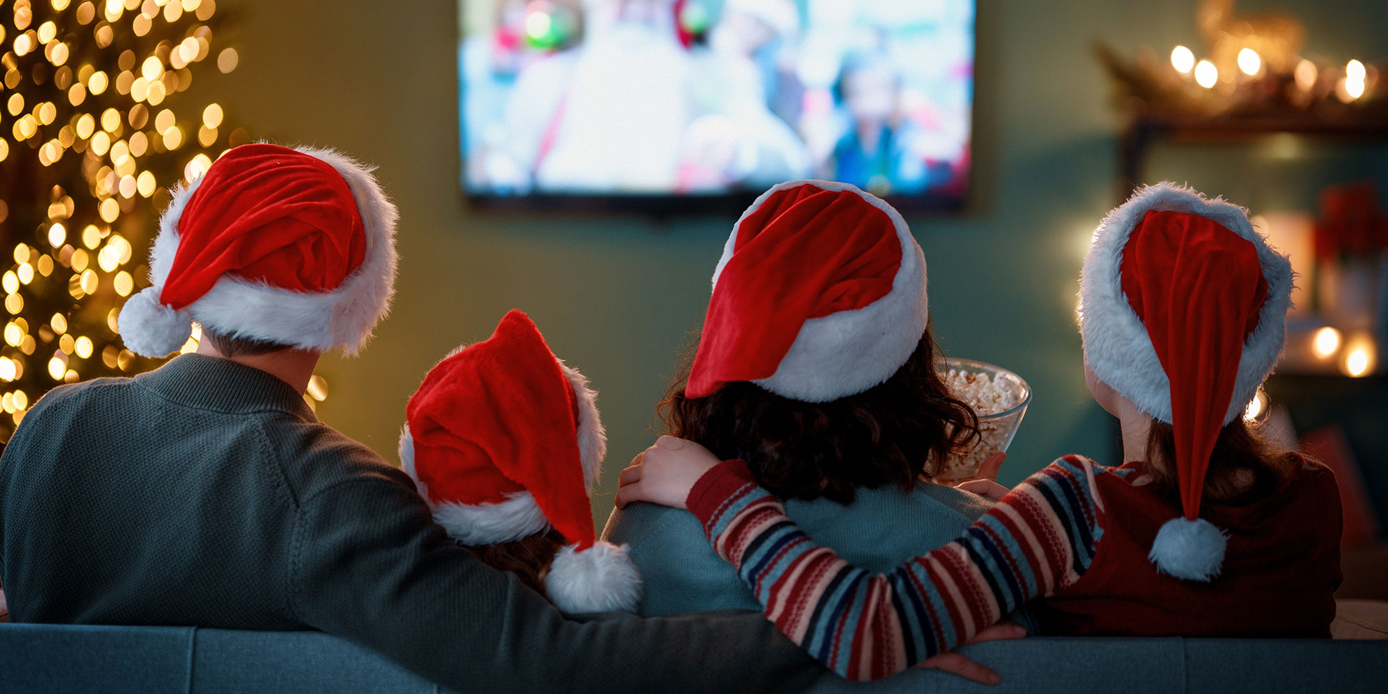 Family wearing Santa hats sitting and watching TV.